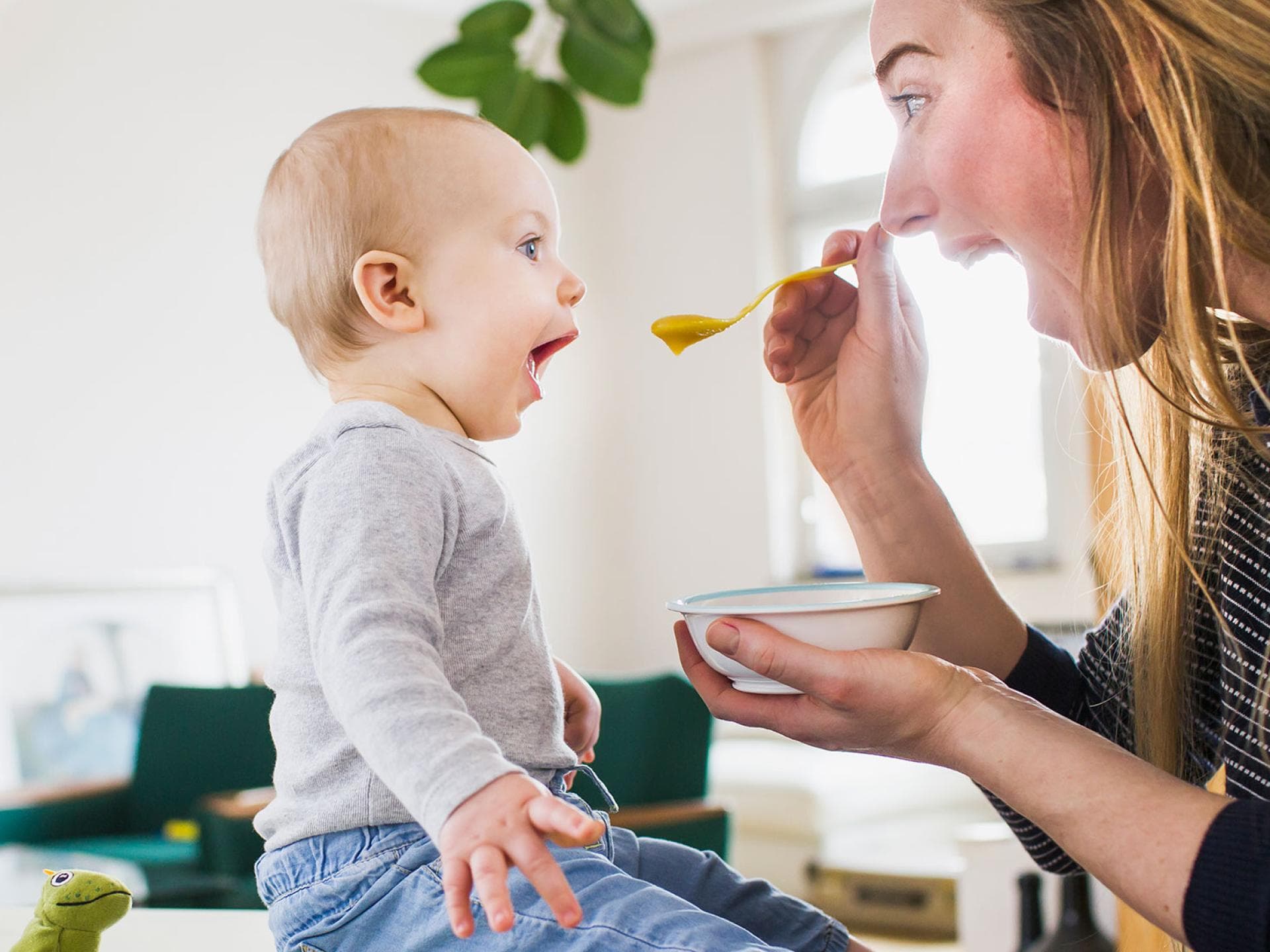 Der erste Brei sollte nicht völlig willkürlich gegeben werden. Hier kommt ein Beikostplan für Babyeltern. Mama füttert Baby mit Brei. Beide sperren den Mund auf.