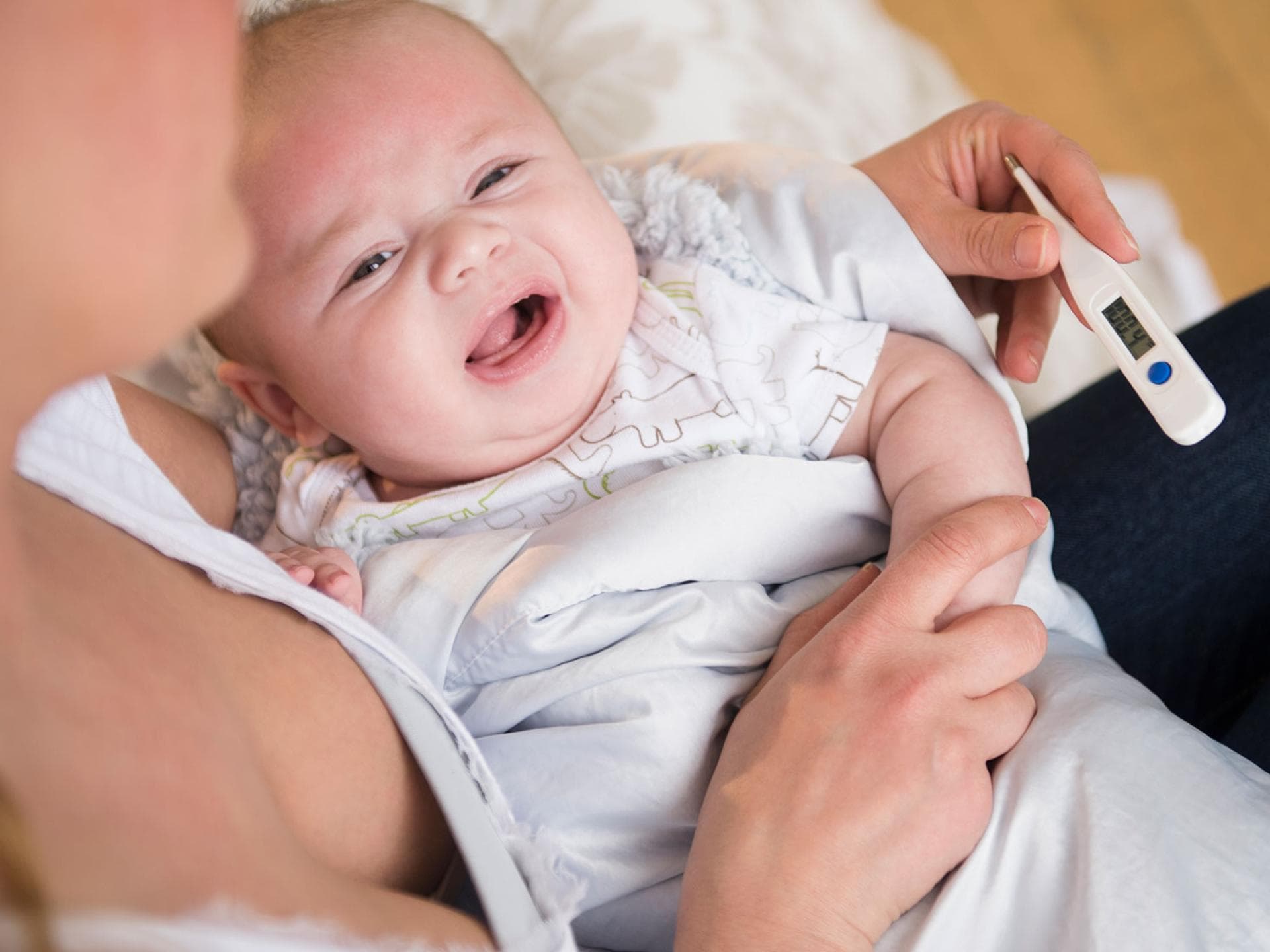 Wenn das Fieber nicht runter geht, machen viele Eltern sich Sorgen um ihr Kind. Eine Mutter misst bei ihrem weinenden Baby mit einem Fieberthermometer die Temperatur.