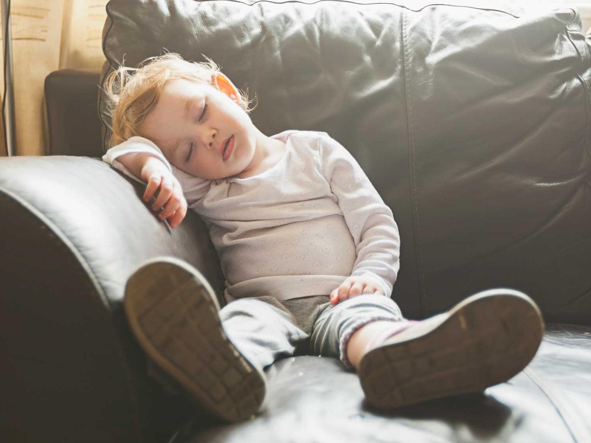 Wenn der Vormittagsschlaf fehlt, kann der Mittagsschlaf die Kleinen vor lauter Müdigkeit überfallen. Ein Kleinkind, das auf dem Sofa einschläft.