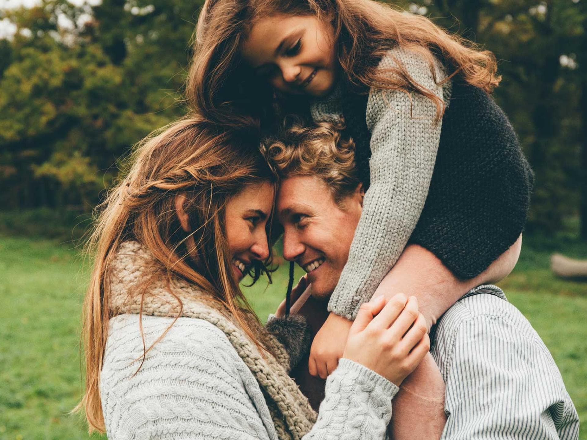 Zeit als Paar? Im Familienchaos manchmal nicht ganz einfach zu finden... Ein junges Pärchen schaut sich in die Augen, während die gemeinsame Tochter auf den Schultern des Vaters sitzt.