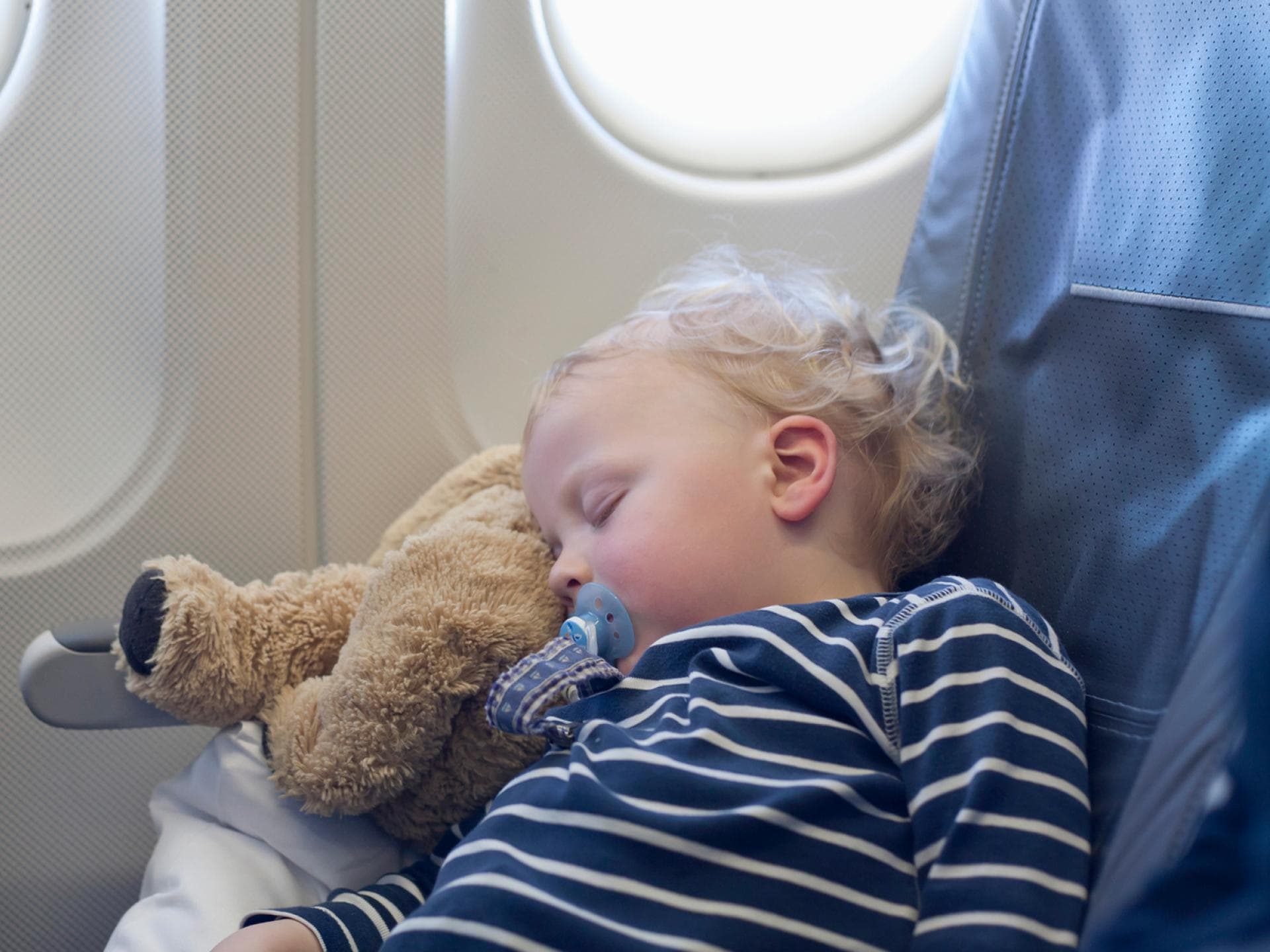 Dank Sitzverlängerung können Kinder im Flugzeug bequem schlafen. Ein kleiner Junge schläft im Flugzeug.