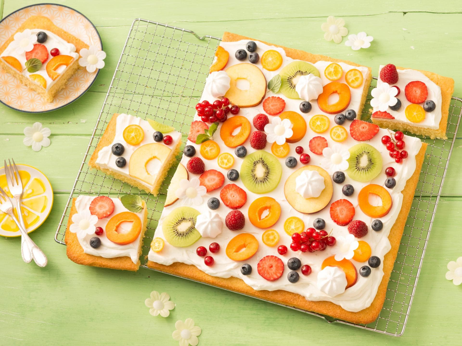 Verteilt ihr verschiedene Obstsorten auf dem Fantakuchen, entsteht eine Obstwiese. Auf einem Blech-Fantakuchen ist verschiedenes Obst verteilt.