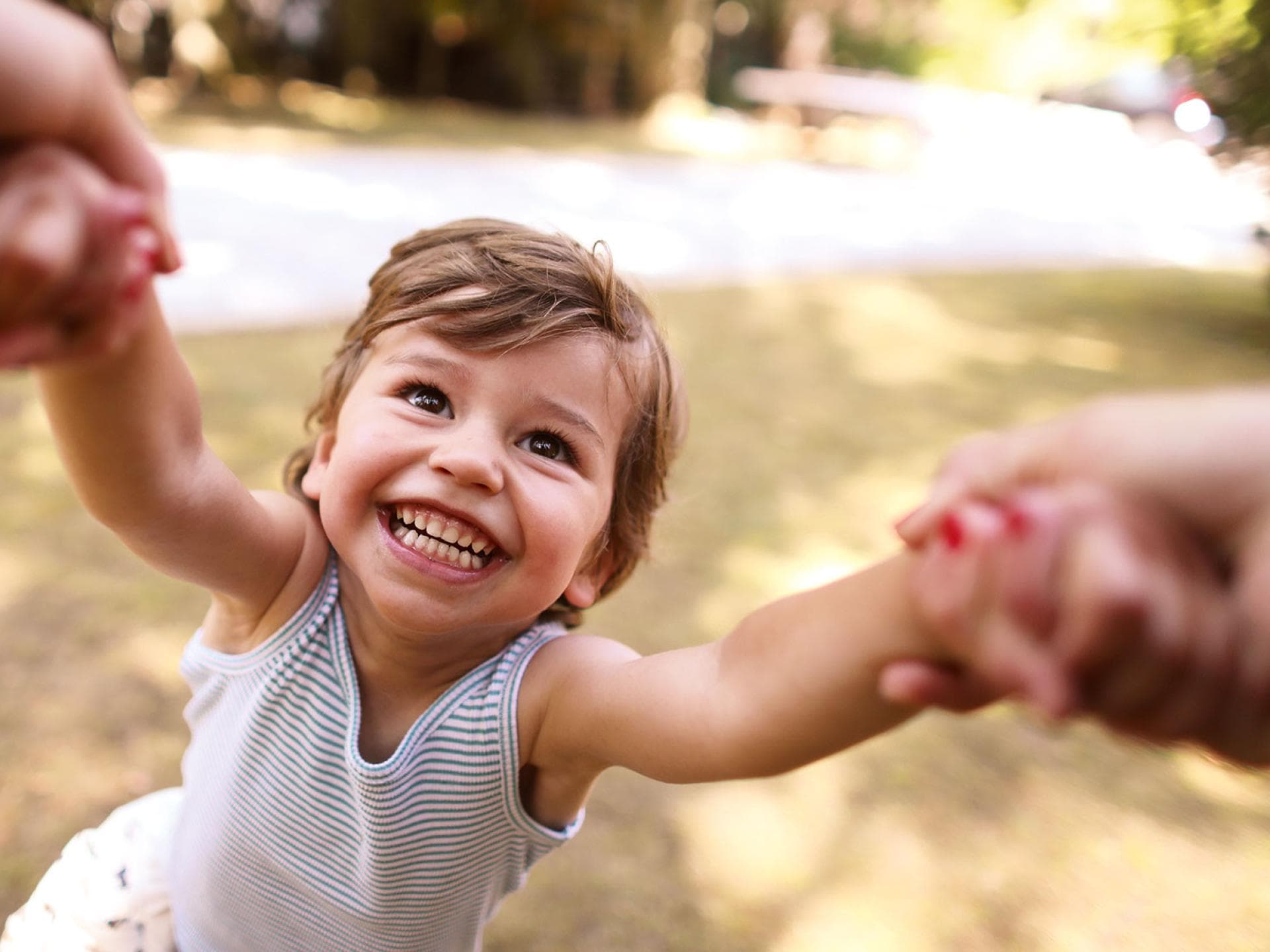 Mimik und eine ausgeprägte Fähigkeit zur Kommunikation mit der Umwelt zeichnen starke Kinder aus. Fröhliches Kind hält die Hände der Eltern.