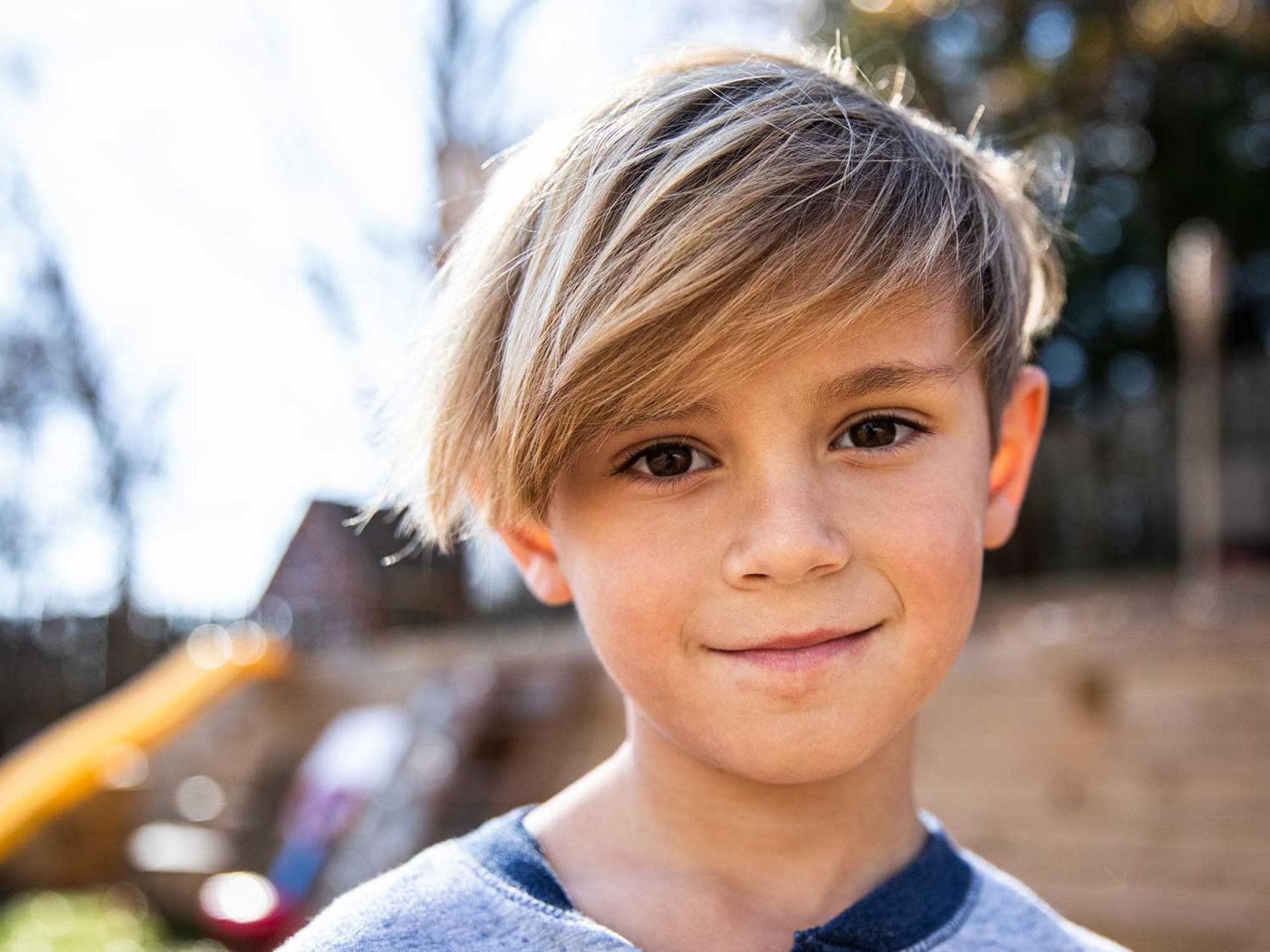 Jungs-Frisuren: Inspirationen für den Friseur-Besuch Blonder Junge mit längeren Haaren lächelt.
