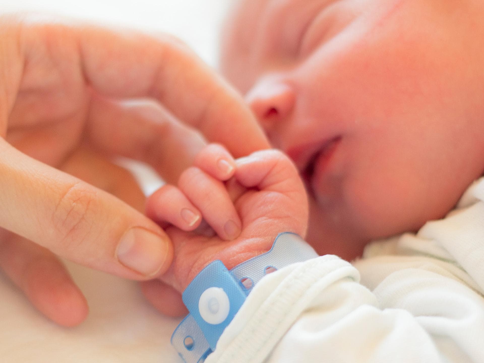 Wenn ein Baby geboren wird, werden gerne Glückwünsche zur Geburt geschickt. Eine Mama streichelt die Hand ihres neugeborenen Babys